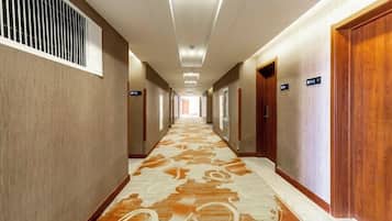 A hotel corridor with carpeted floors, wooden doors, and directional signs.