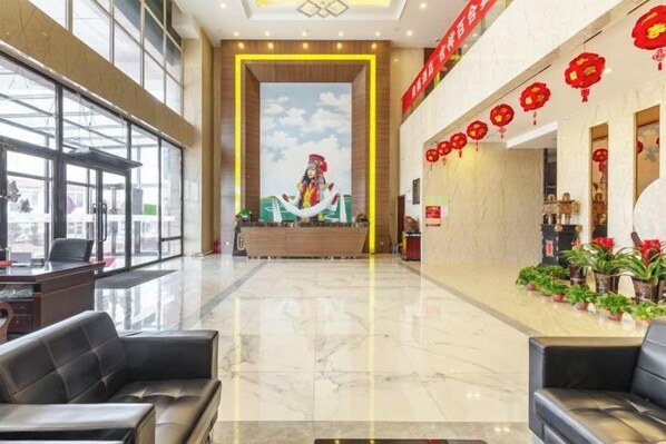 A hotel lobby with a reception desk, seating area, and potted plants. - Huangsheng Hotel (Wuchuan)