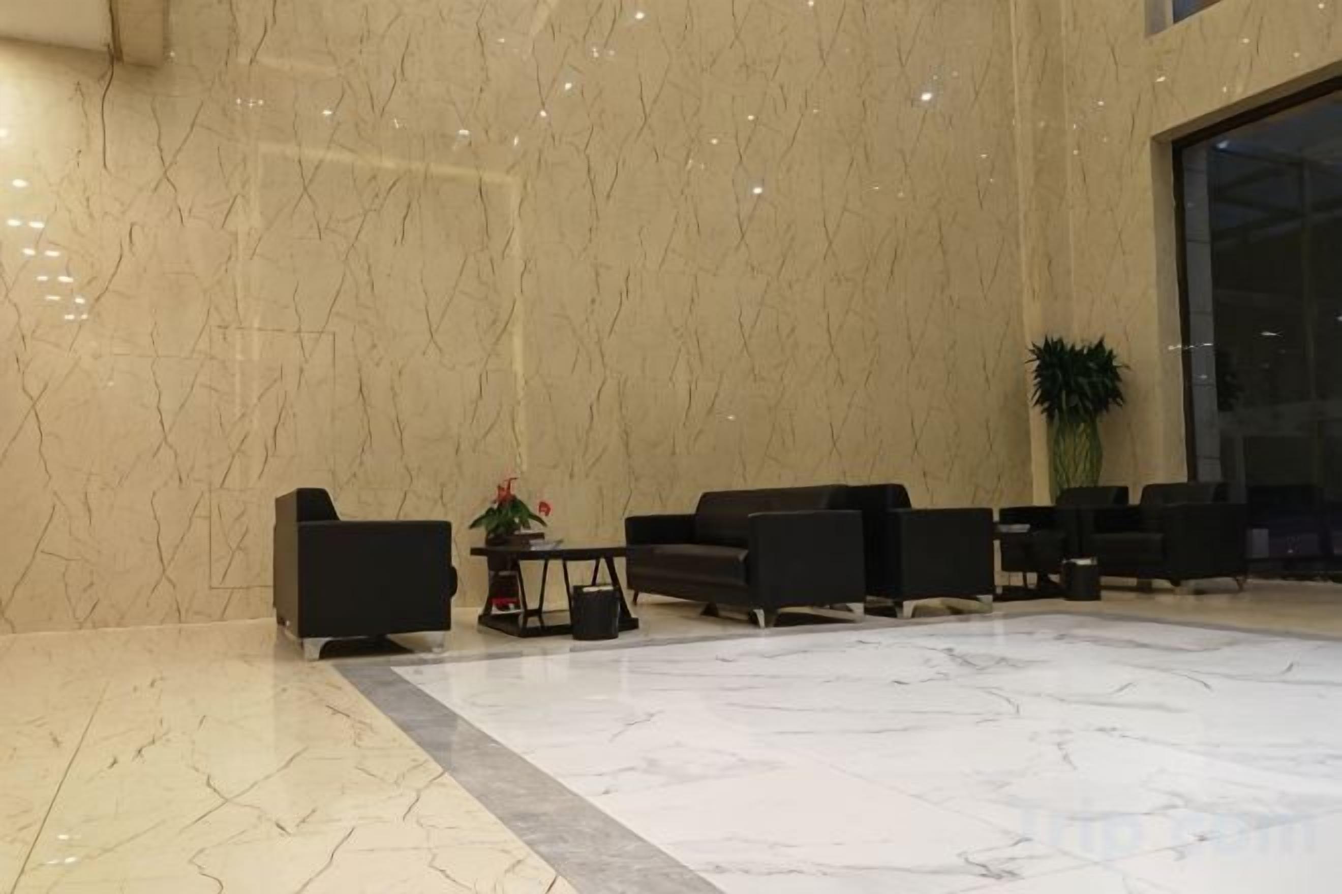 A lobby with marble walls and floor, black seating, a small table with a plant, and a large window.