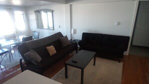 A living room with a sofa, a coffee table, and a dining table. - Direct ocean view 2 bed 2 bath 36 ft deck walk to beach. (Hull)