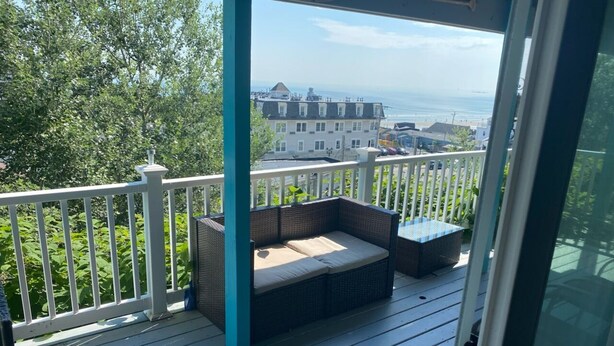 A covered outdoor deck with a sofa and cushions, overlooking a residential area and the ocean. - Direct ocean view 2 bed 2 bath 36 ft deck walk to beach. (Hull)