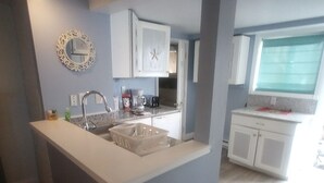 A kitchen with a central island, white cabinets, a sink, and a window with a view. - Direct ocean view 2 bed 2 bath 36 ft deck walk to beach. (Hull)