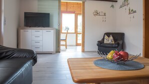 A living room with a television, a sofa, a dining table with fruit, and a chair. - Apartment 'Kleiner Spatz' with Terrace, Shared Garden & Wi-Fi (Leutkirch im Allgäu)