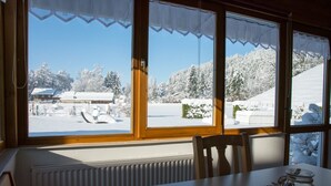 A room with a view of a snowy landscape through large windows, a table, and a chair. - Apartment 'Kleiner Spatz' with Terrace, Shared Garden & Wi-Fi (Leutkirch im Allgäu)