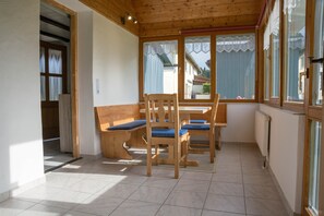 Una habitación con una mesa y sillas de madera, un banco, una ventana con vistas y un radiador.