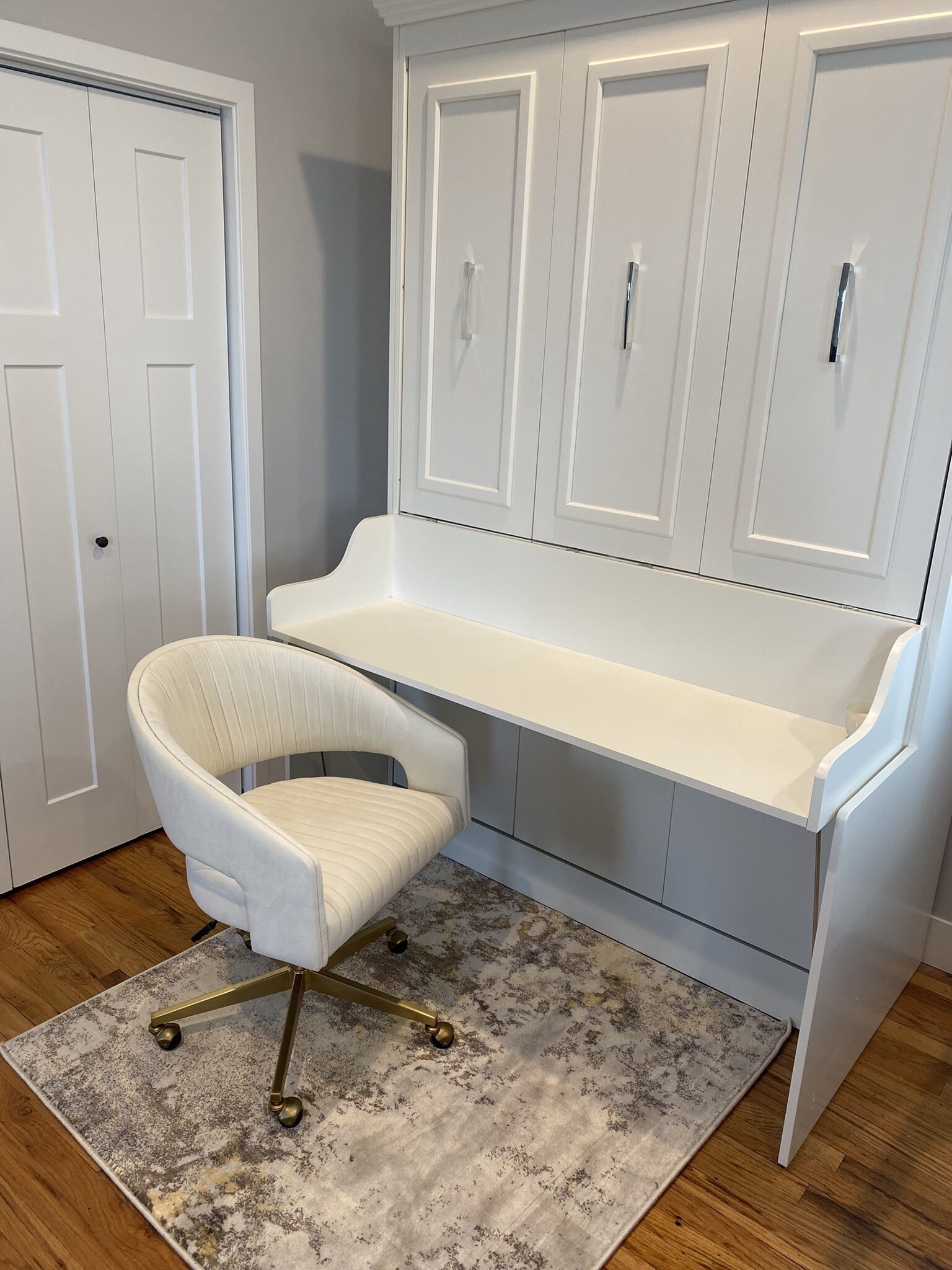 A white desk with a chair, a white door, and a patterned rug.