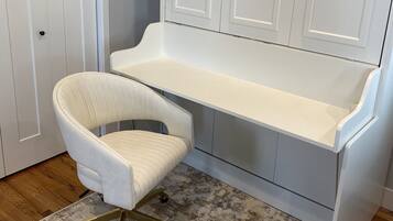 A white desk with a chair, a white door, and a patterned rug.