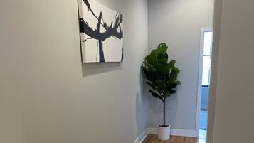 A hallway with a wooden floor, a patterned rug, a large abstract painting, and a potted plant.