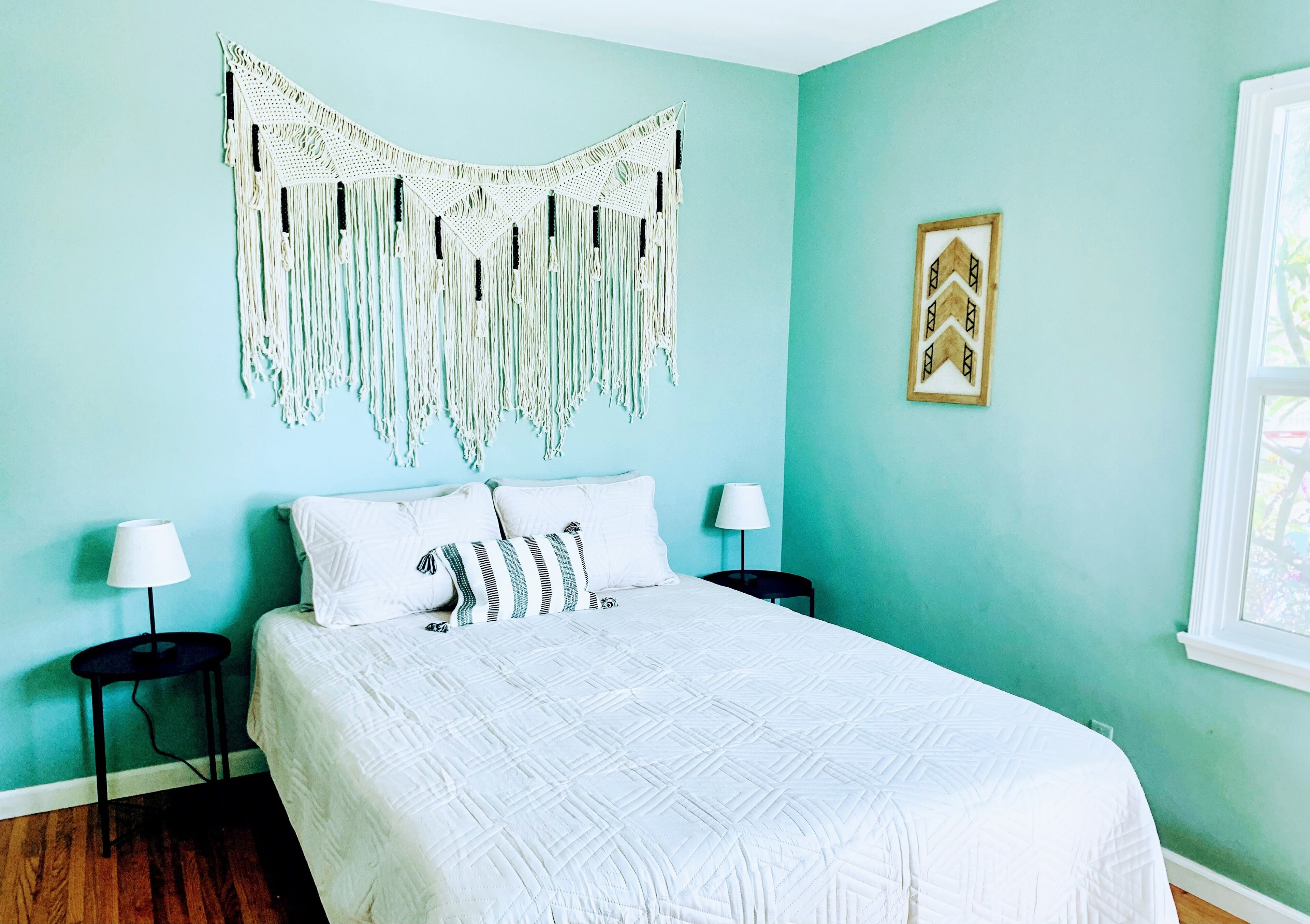 A bedroom with a bed, two bedside tables, a macrame wall hanging, and a framed picture on the wall.