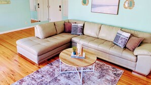 A living room with a beige sectional sofa, a round wooden coffee table, and a patterned rug. - Midtown Ventura Family & Pet Friendly Cottage (Ventura)