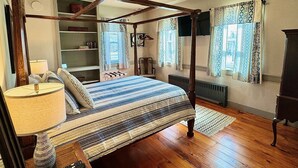 Una cama con dosel, con colcha a rayas, una lámpara de noche y un jarrón decorativo sobre una mesita de madera.