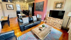 Una sala de estar moderna con un sofá de cuero negro, una mesa de centro de madera y un televisor sobre un mueble de madera.