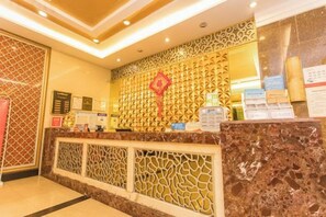 Een hotel receptie met een marmeren balie, decoratieve wandpanelen en een rood accent.