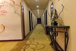 Un couloir d’hôtel orné d’une fresque murale à motifs floraux, avec un comptoir de réception et une moquette à motifs.