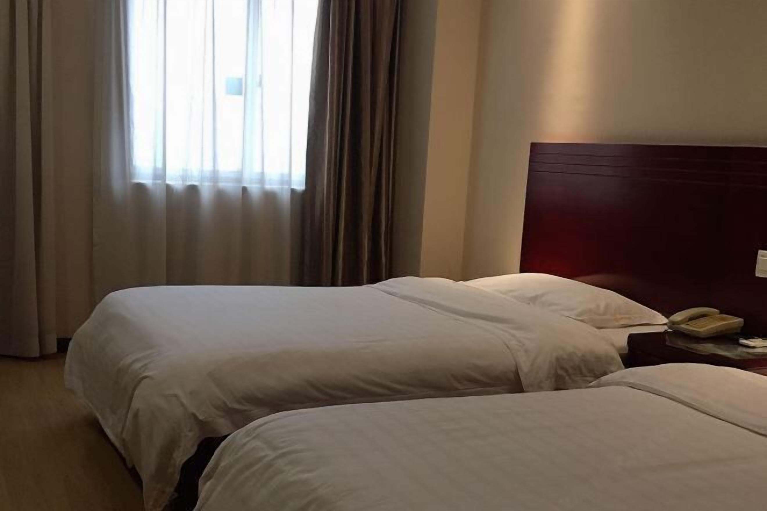 A hotel room with two beds, a wooden headboard, a bedside telephone, and a window with curtains.