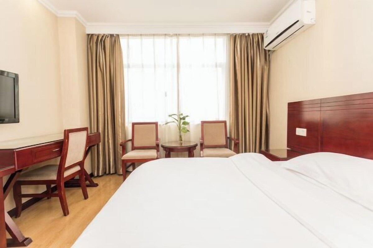 Habitación de hotel con una cama, un escritorio, dos sillas, una mesita y un televisor.