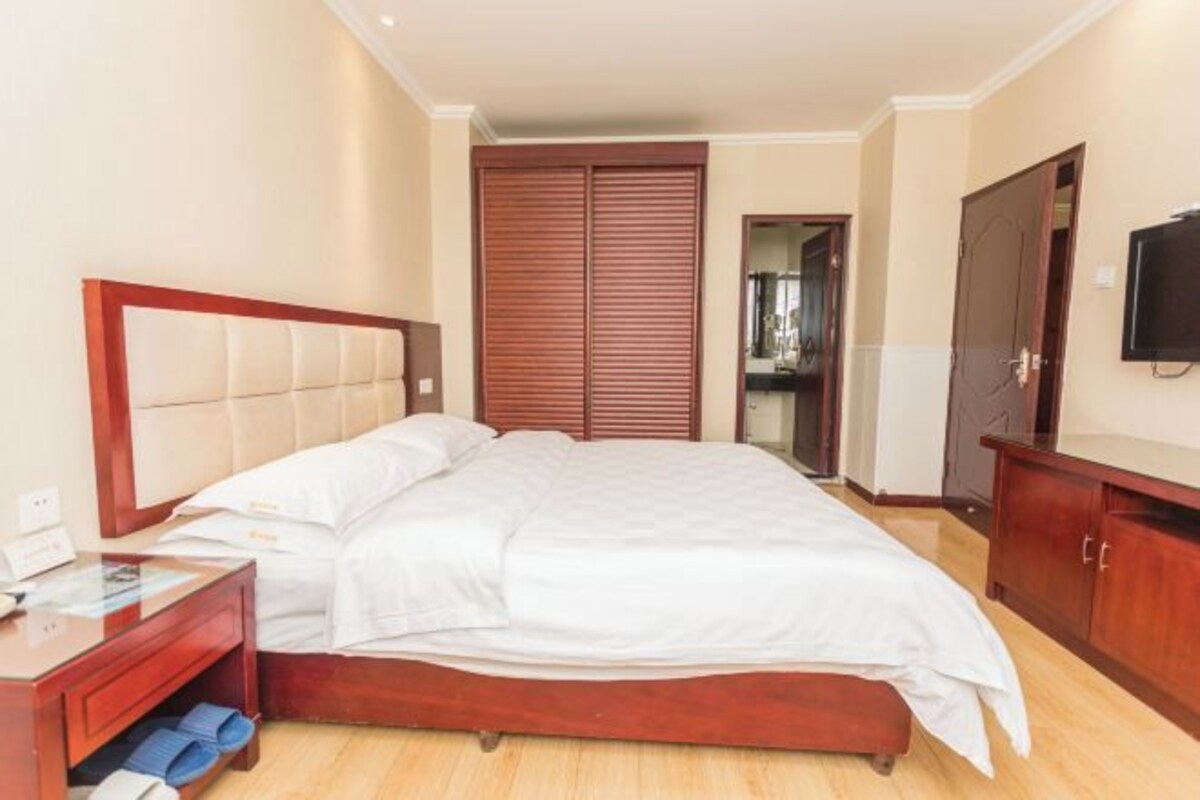 Una camera d'albergo con un letto, un armadio in legno, una TV e un comodino con una lampada.