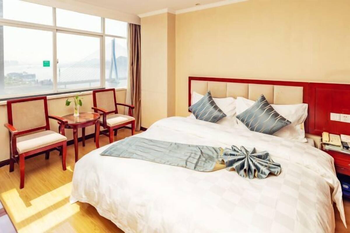 Hotelkamer met een groot bed, een bureau en stoelen, een raam met uitzicht en een rode hoofdeinde.