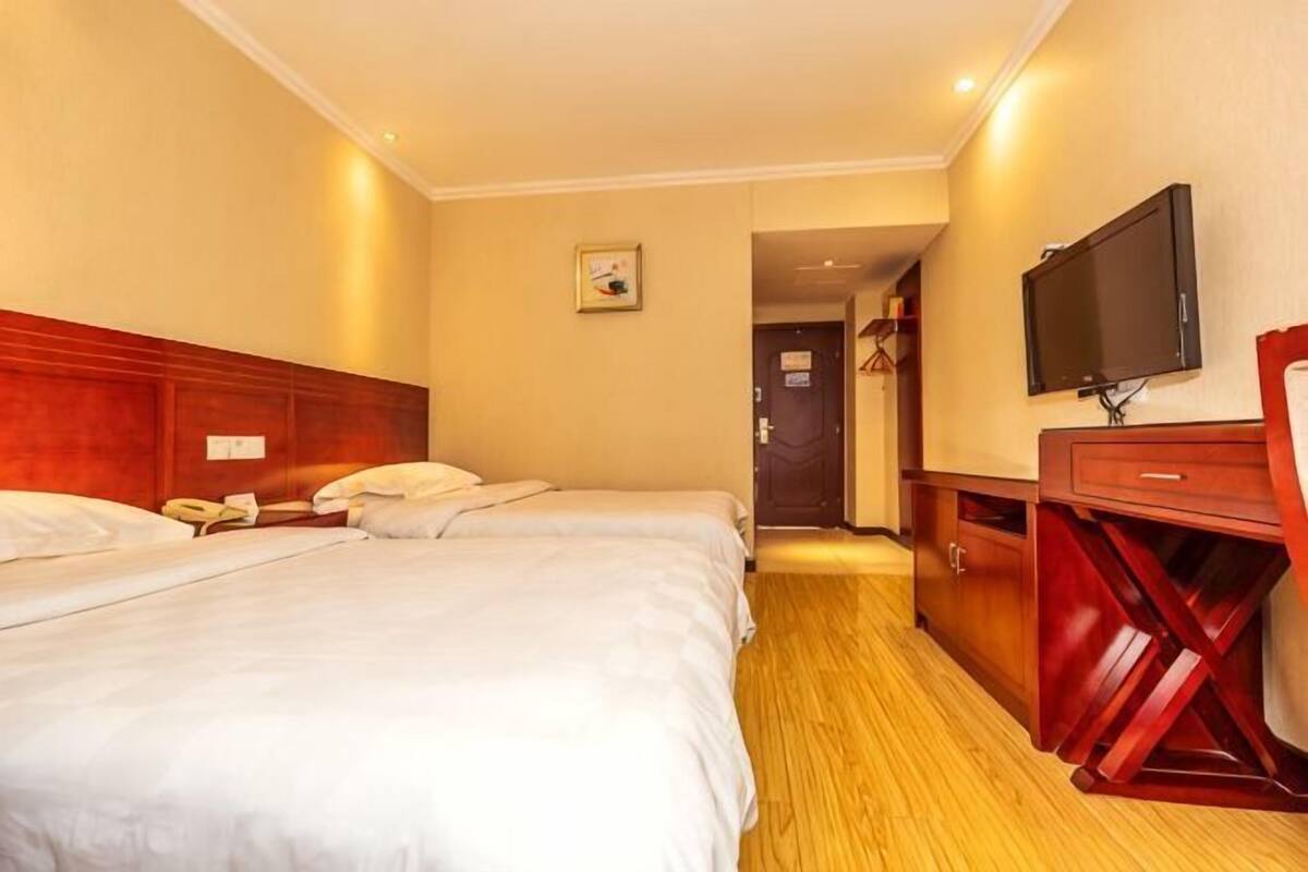 Een hotelkamer met twee bedden, een houten bureau, een televisie en een deur naar een andere kamer.
