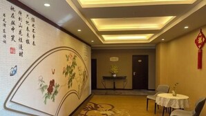 Een hotellobby met een decoratieve muur, een receptiebalie en een zithoek met tafels en stoelen.