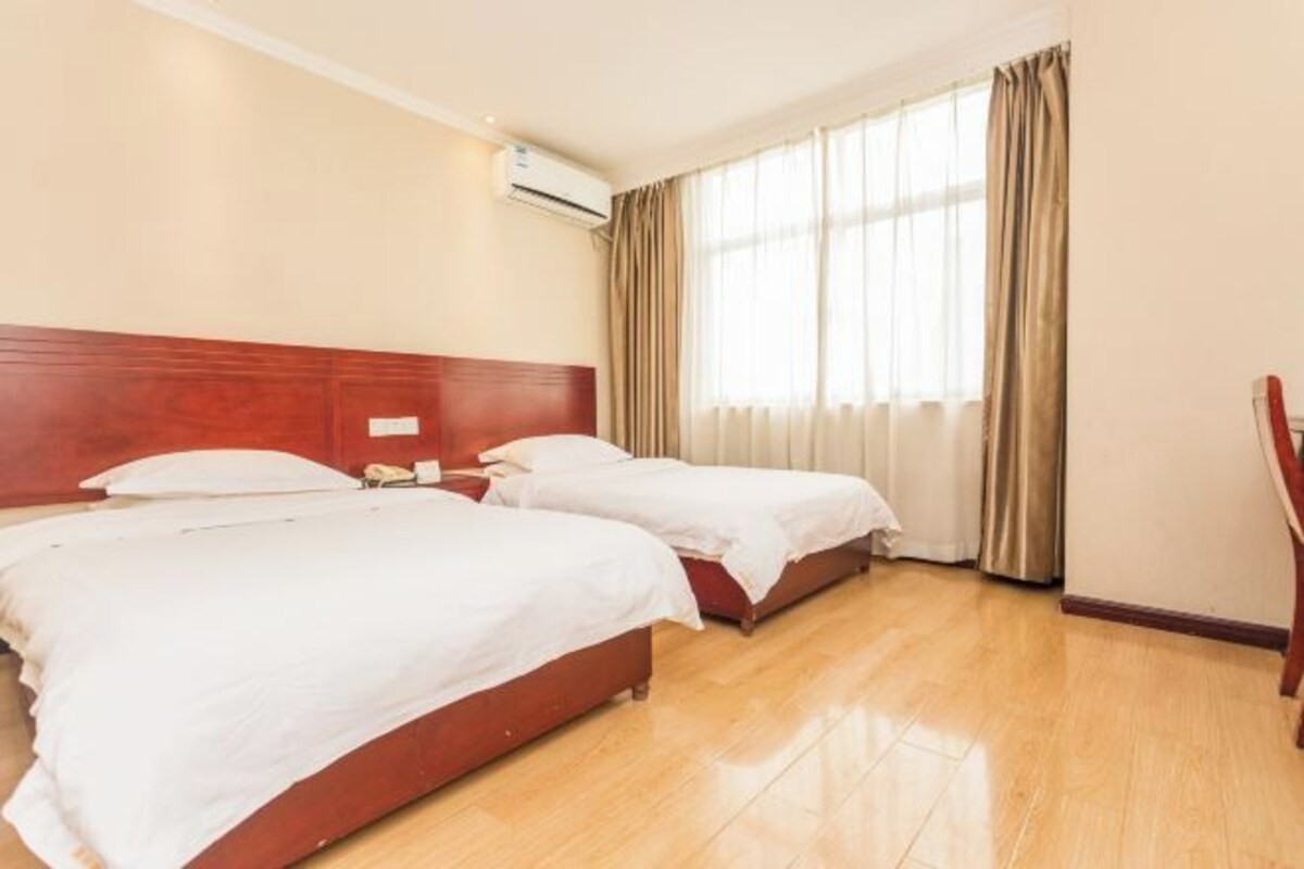 Una camera d'albergo con due letti, una testiera in legno, una finestra con tende e un pavimento in legno.