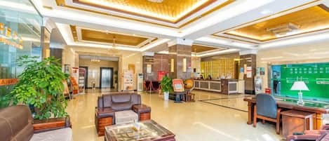A spacious lobby with a reception desk, seating area, and a green screen displaying information.