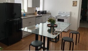 A modern kitchen with a glass island table, black stools, a black refrigerator, a white stove, and white cabinets.