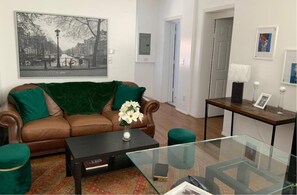A living room with a brown leather sofa, green cushions, a glass coffee table, and a black side table.