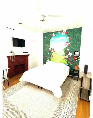 A bedroom with a bed, a dresser, a TV, and a wall mural.