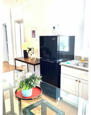 A modern kitchen with a black refrigerator, white cabinets, and a glass table with a potted plant.