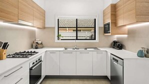 A modern kitchen with white cabinetry, a gas stove, a dishwasher, and a window with a view of the outside. - Stroll to beach, cafes & restaurants (BOOKER BAY)
