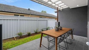 A patio with a wooden table and chairs, a metal fence, and a grey tiled floor. - Stroll to beach, cafes & restaurants (BOOKER BAY)