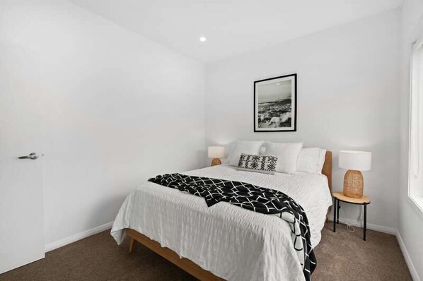 A bedroom with a bed, two bedside lamps, a framed picture on the wall, and a door.