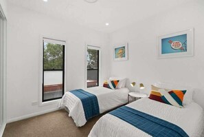 Two single beds with white bedding and blue accents, each with a bedside table and lamp, offer a functional workspace.