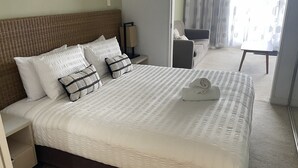 Habitación de hotel con una cama grande, dos almohadas, una mesita de noche, una lámpara, una silla y vistas al exterior a través de una ventana.