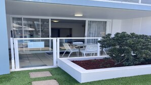 Un edificio moderno con puerta de vidrio que da a un balcón con sillas y mesa blancos.