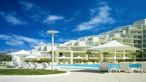 Un hotel con zona de piscina, tumbonas, sombrillas y un cielo azul despejado.