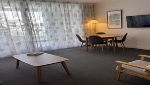 Habitación de hotel con un ventanal grande, una mesa, sillas, una lámpara y un televisor en la pared.