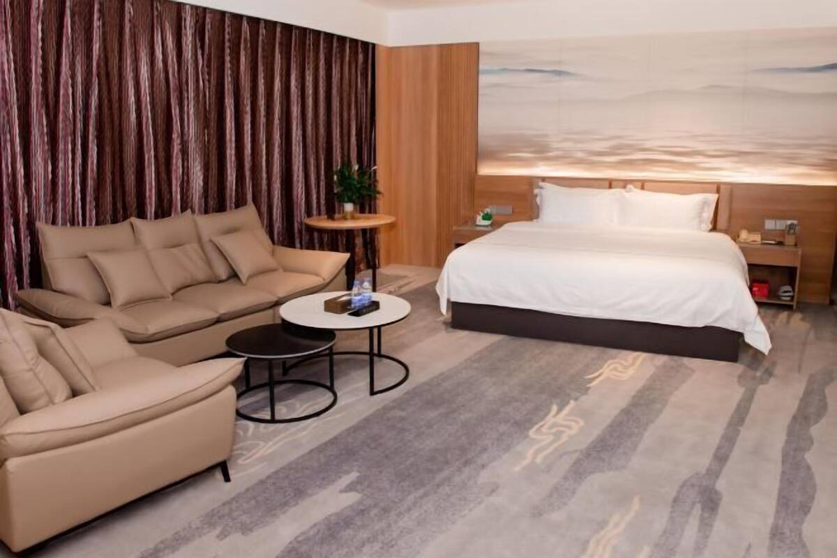 A hotel room with a large bed, a sofa, a small round table, and a nightstand.