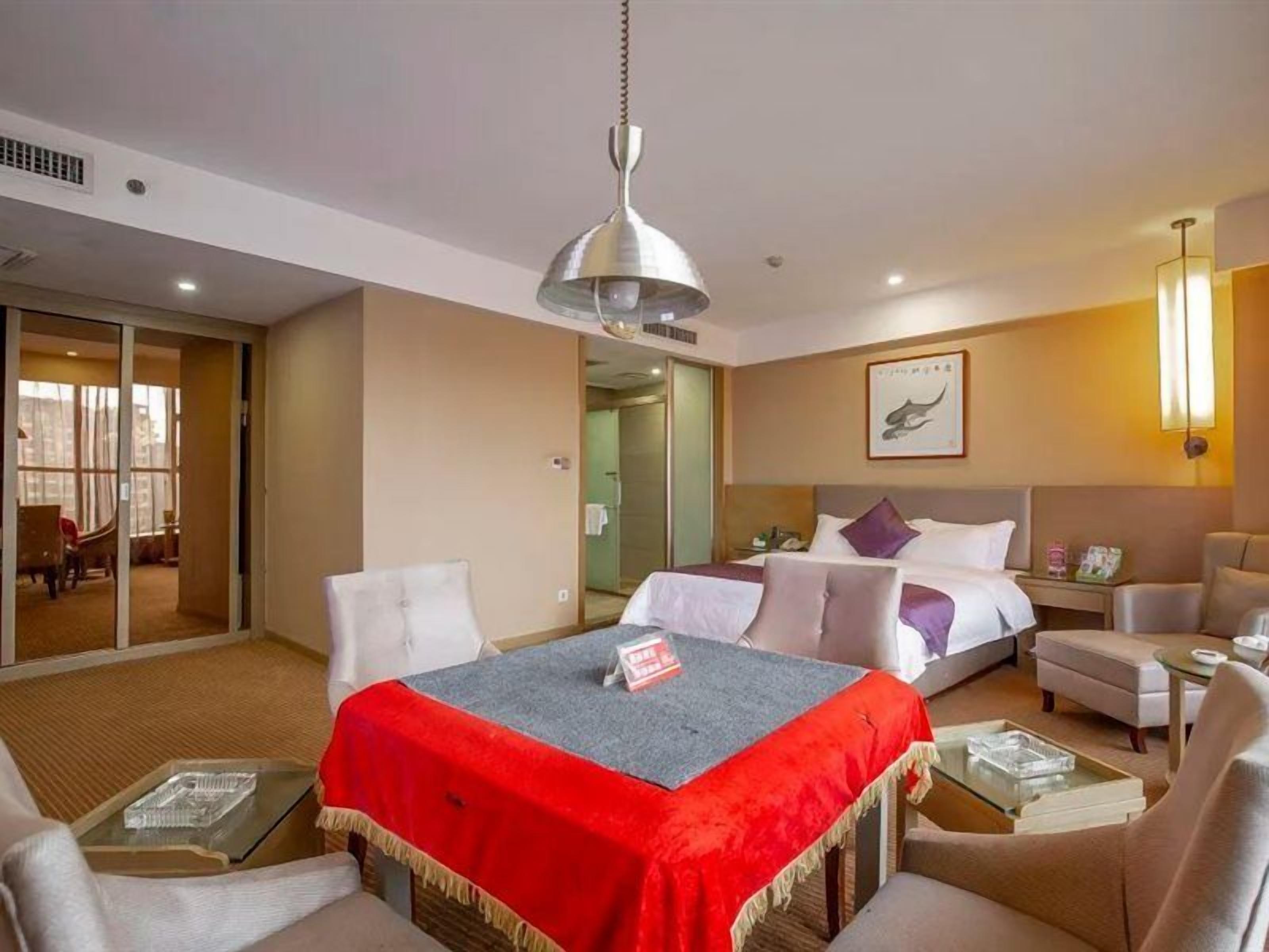 A hotel room with a bed, a desk, a chair, a sofa, and a dining table.