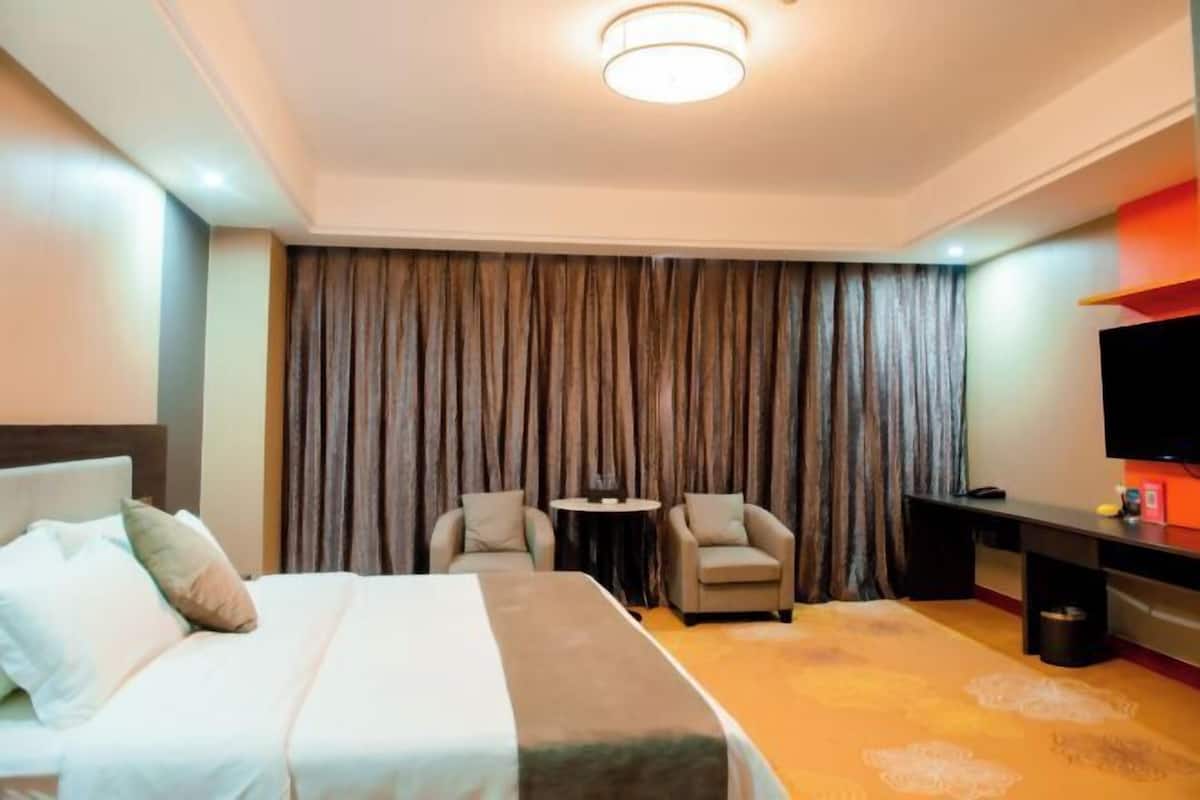 A hotel room with a bed, two armchairs, a small table, a TV, and a curtain backdrop.