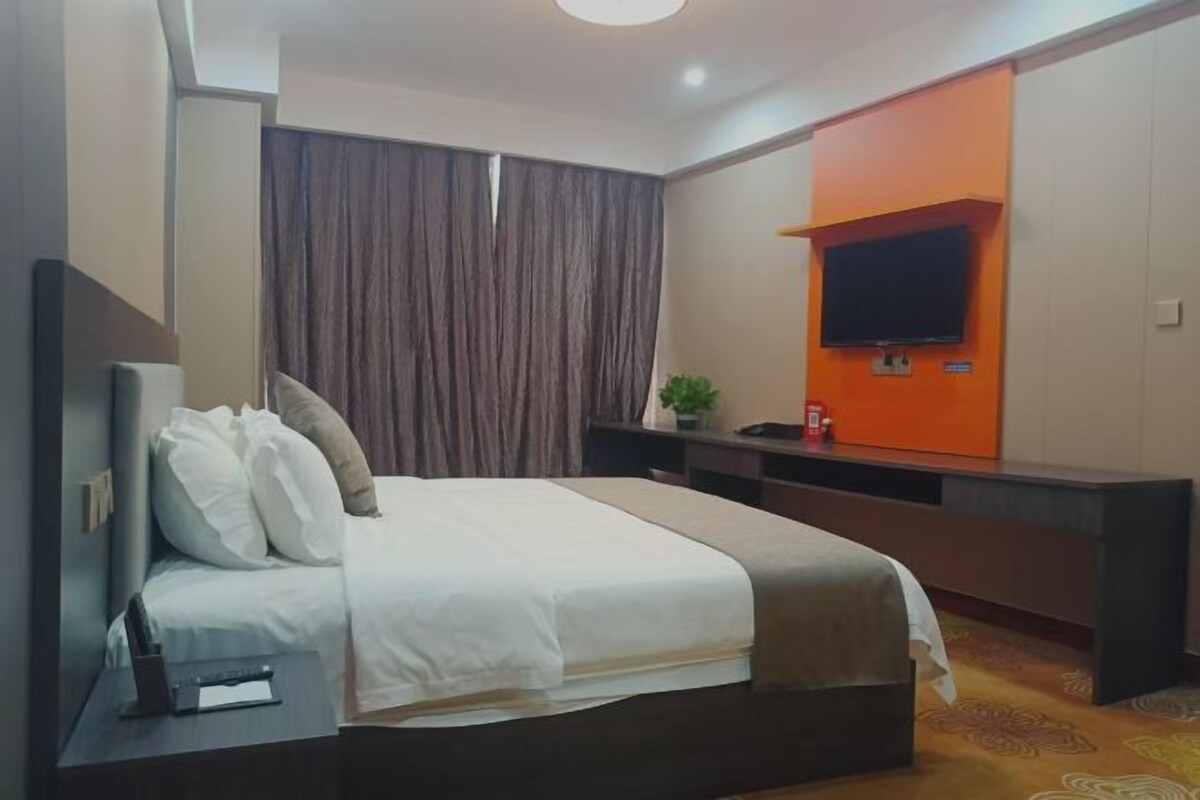 A hotel room with a bed, a desk with a TV, and a curtain.