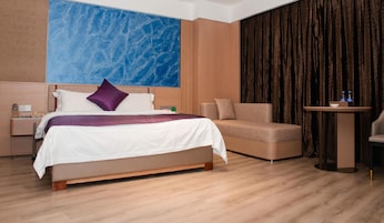 A hotel room with a bed, a sofa, a small table, and a large window with curtains.