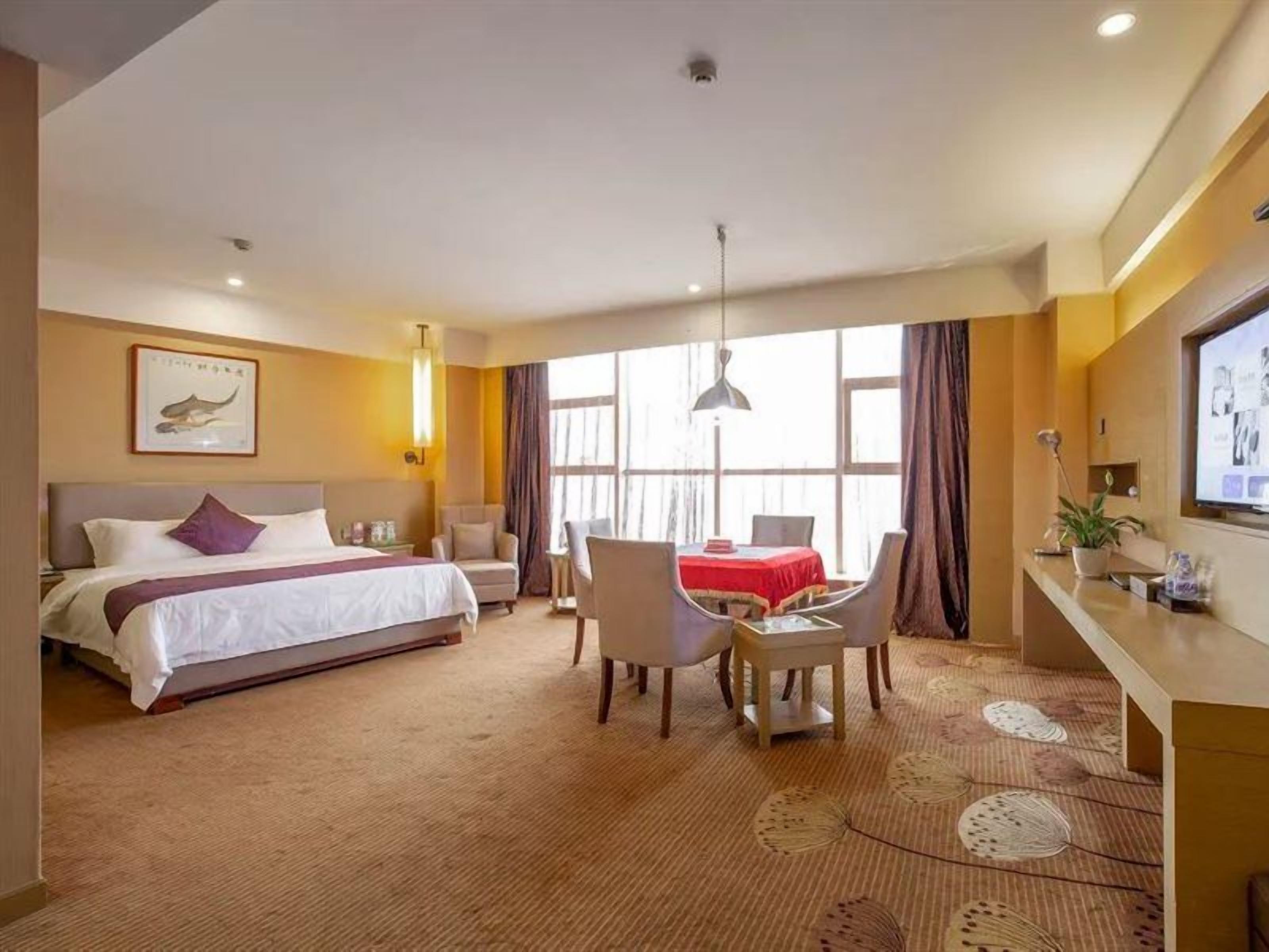 Une chambre d’hôtel avec un lit, un bureau, une chaise, une télévision et une grande fenêtre.