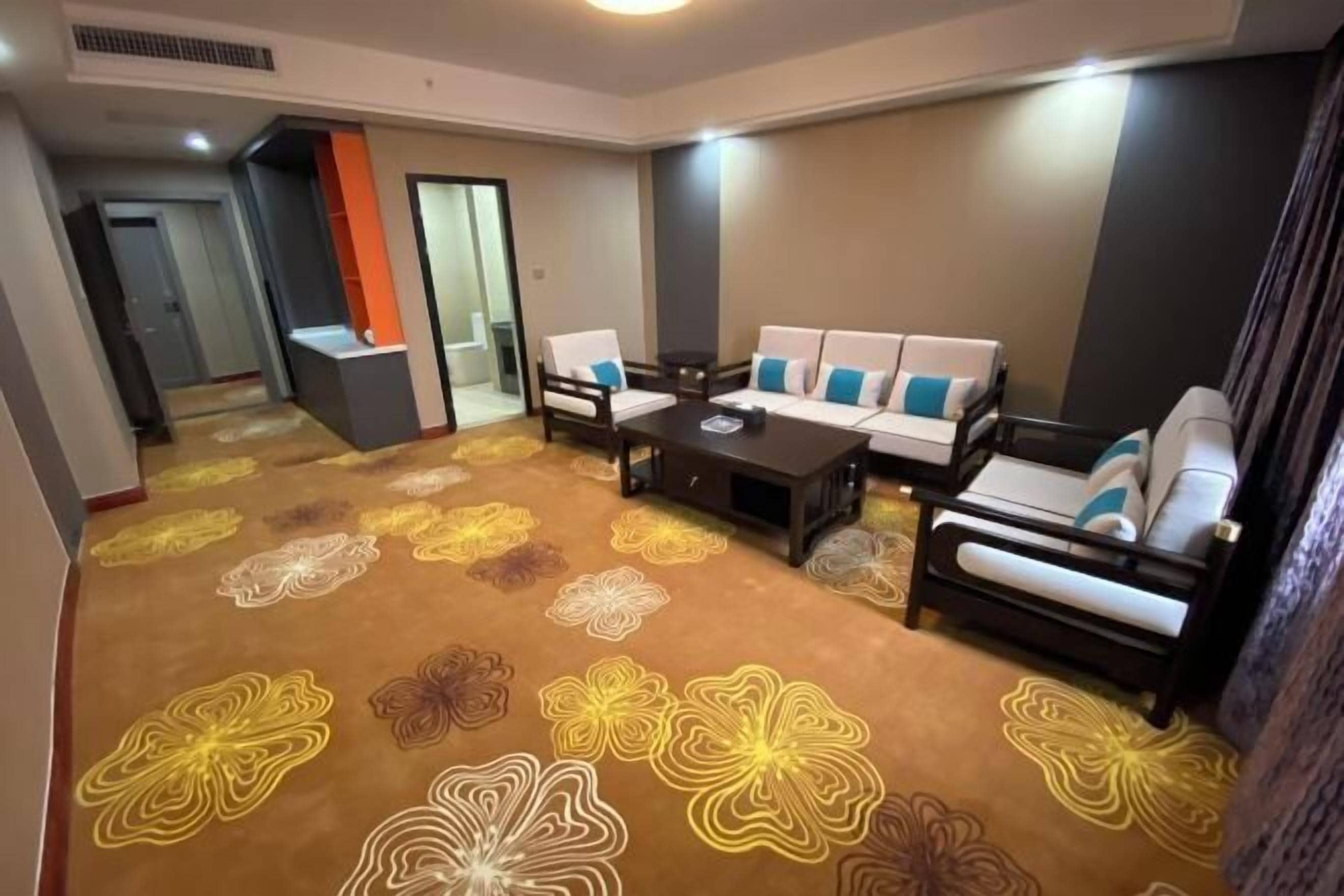 Een hotelkamer met een zithoek, een bijzettafeltje en een vloerkleed met bloemenmotieven.