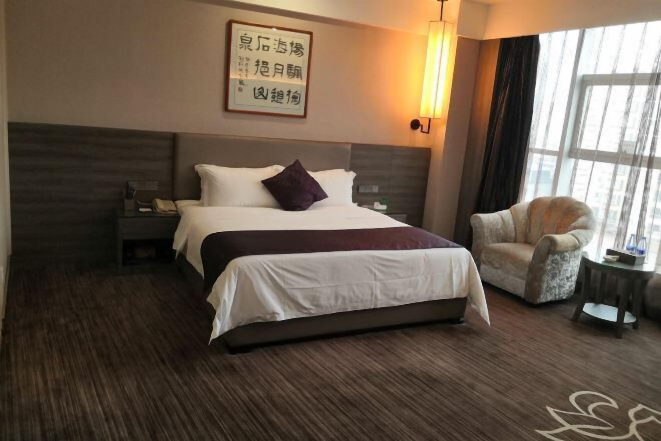 A hotel room with a large bed, bedside tables, a chair, and a window with curtains.