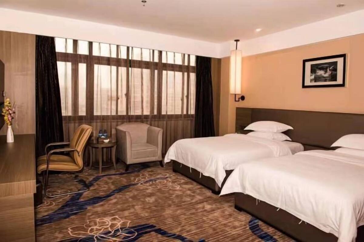 A hotel room with two beds, a desk, a chair, a small table, and a large window with curtains.