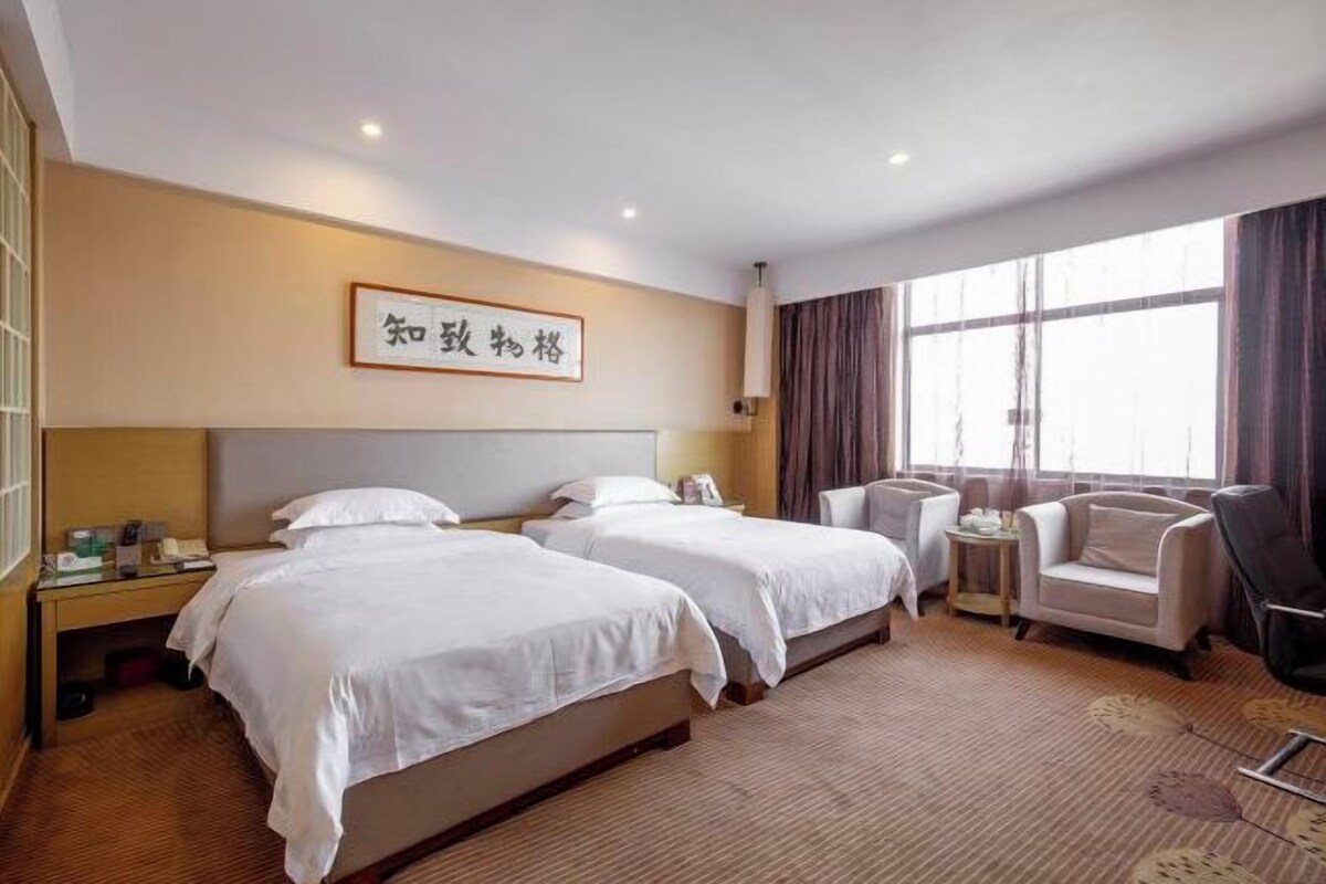A hotel room with two beds, a sofa, a small table, and a large window with curtains.