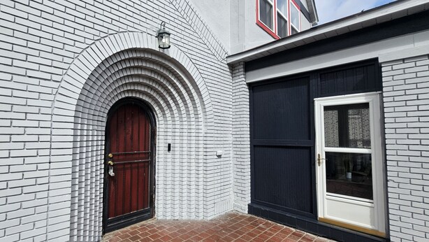 Un edificio con fachada de ladrillo, puerta roja y ventana con marco negro.