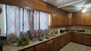 Una cocina con armarios de madera, encimeras de granito, un lavamanos y una zona de comedor con mesa y sillas.